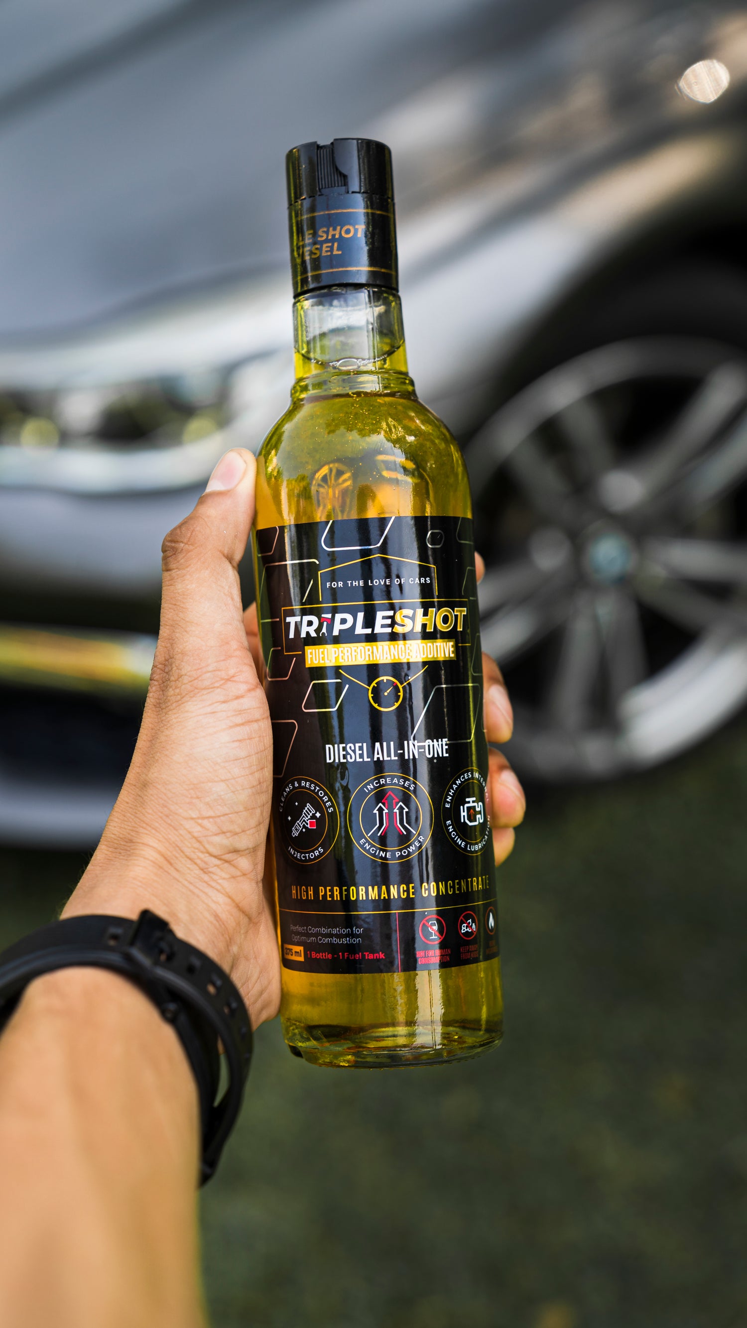 Hand holding a bottle of 'Triple Shot' diesel engine treatment with a car in the background.
