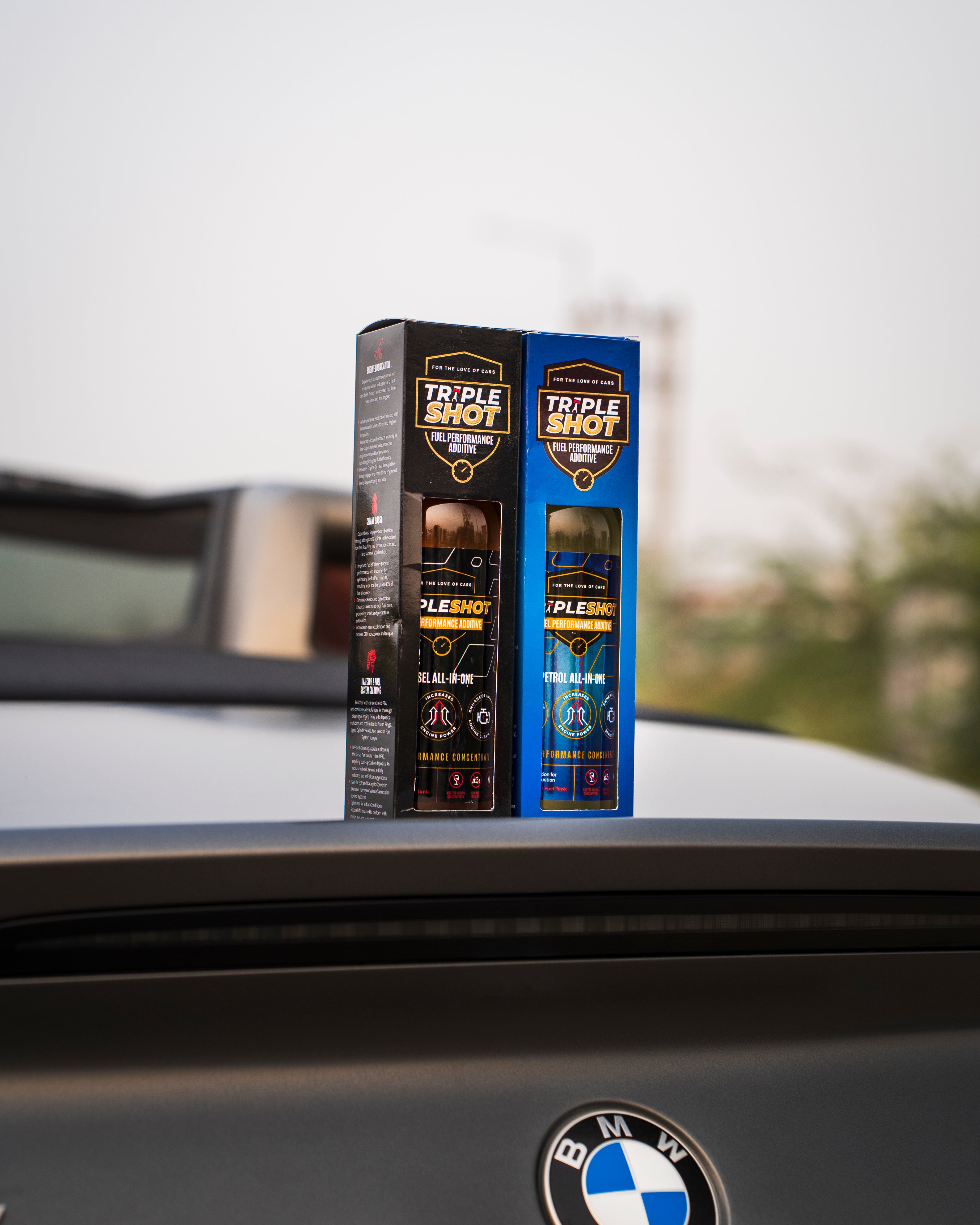 Tripleshot Fuel Performance Additive boxes for diesel and petrol engines placed on the rear of a BMW convertible, with the car's logo and soft top roof partially visible in the background.