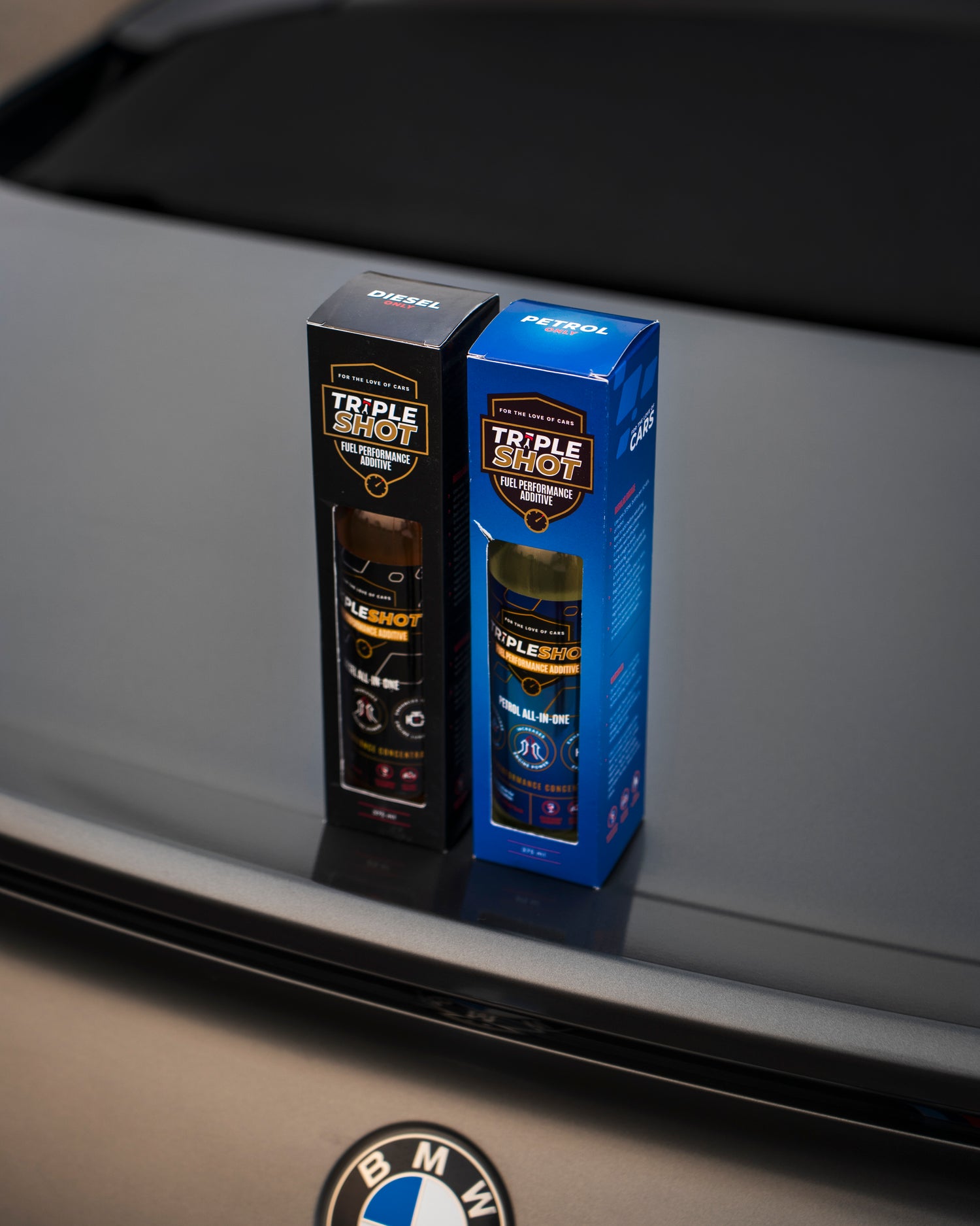 Two boxes of Tripleshot Fuel Performance Additive, one for diesel and one for petrol, placed on the trunk of a BMW car. The packaging highlights the product’s high-performance formula for improved engine efficiency.