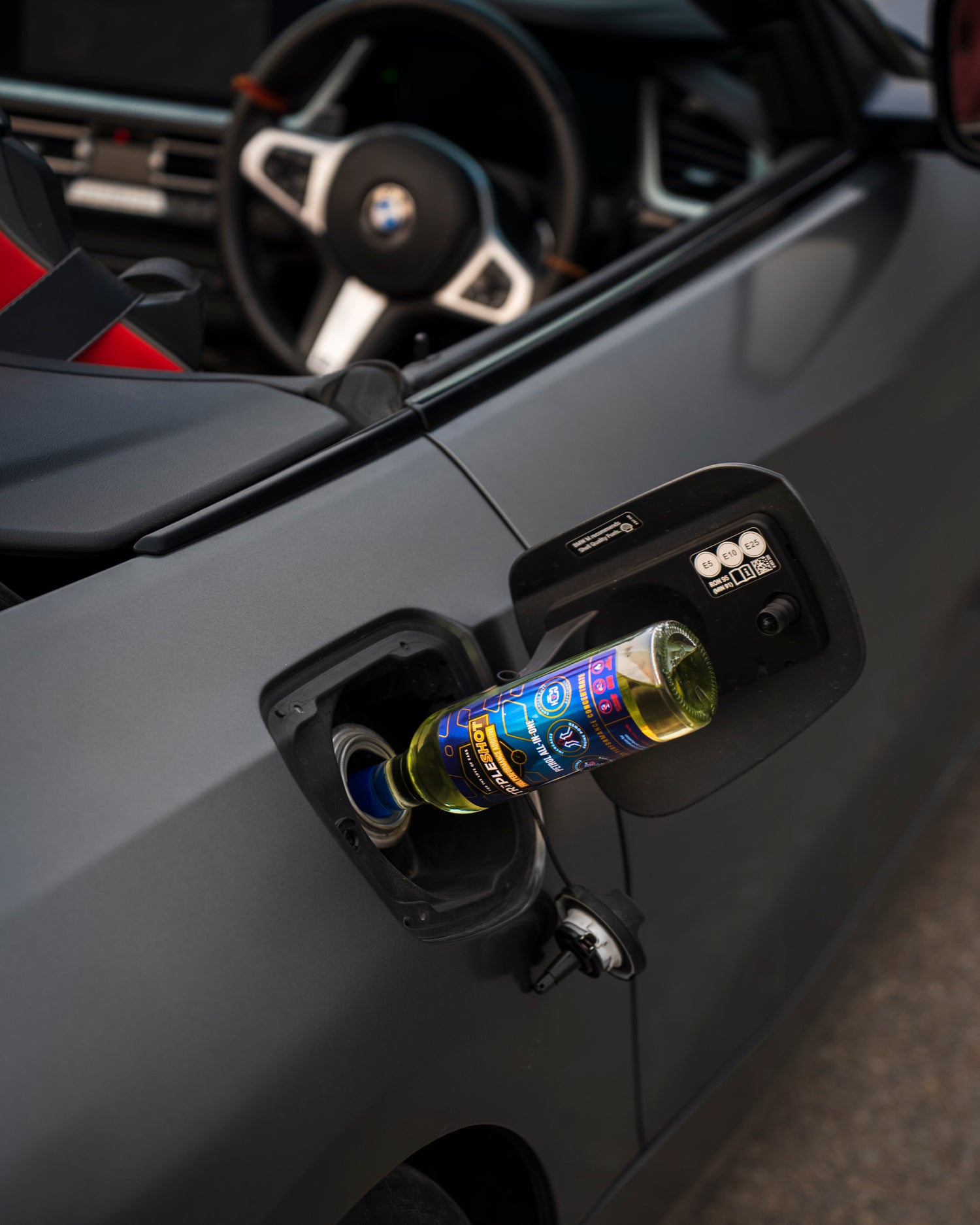 Tripleshot Petrol All-In-One Fuel Performance Additive bottle inserted into the fuel tank of a BMW convertible, showcasing product application during refueling.