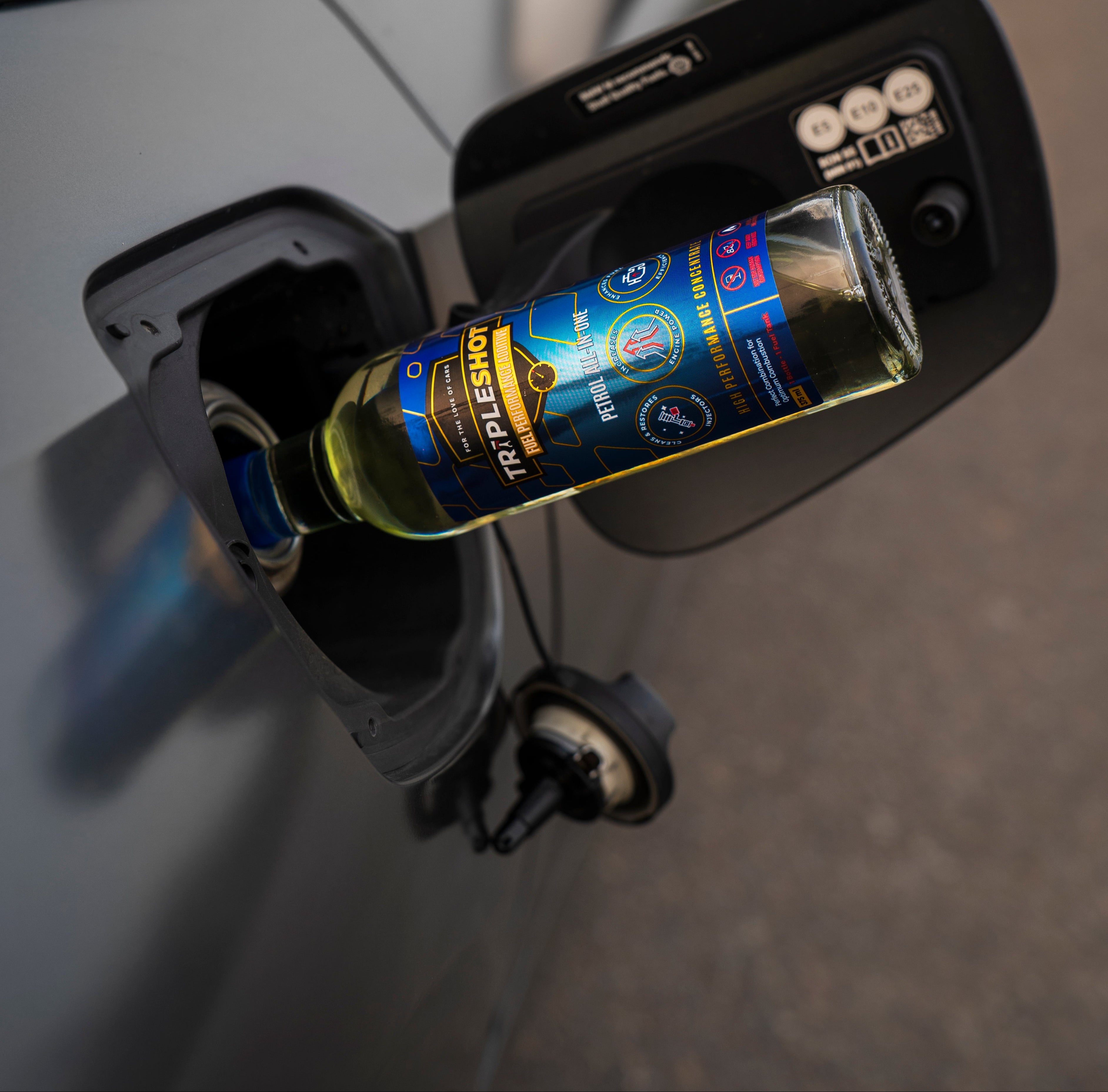 Bottle of fuel additive being poured into a car's fuel tank.